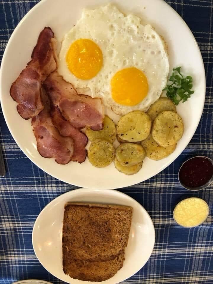 Two fried eggs with bacon, sautéed potatoes and brown toast