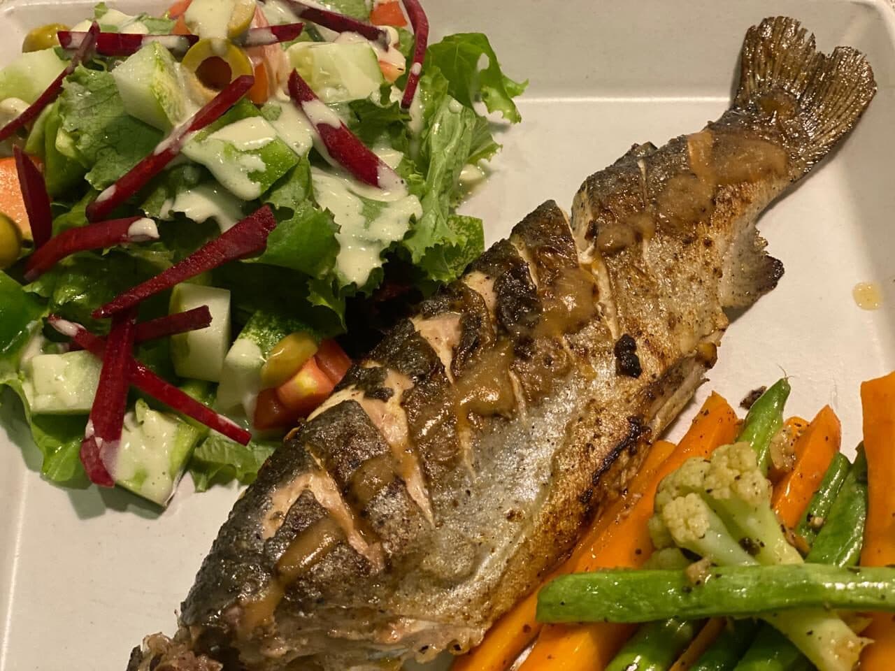 Whole grilled rainbow trout with salad and vegetables