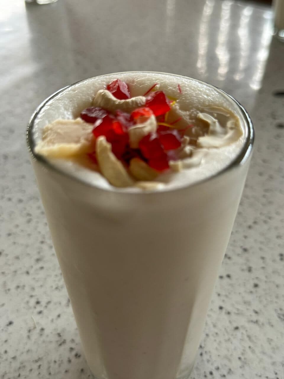 A tall glass of lassi topped with cherries and nuts