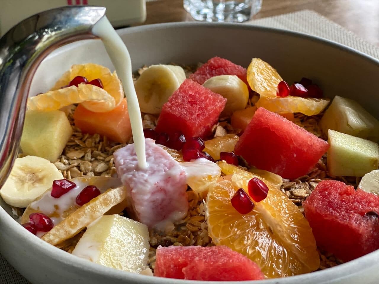 Milk poured over muesli with watermelon, orange and banana