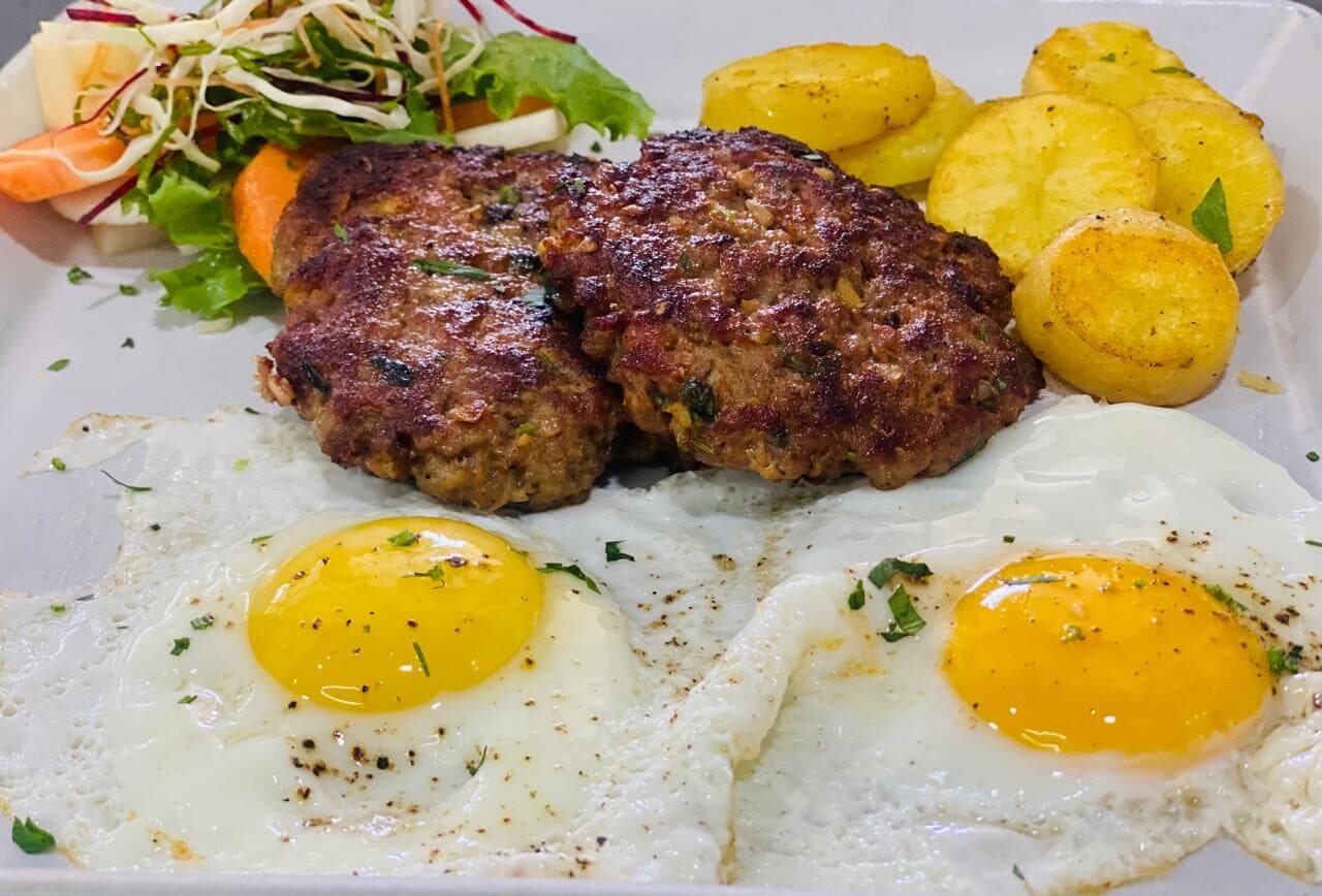 Grilled patties with fried eggs and golden potatoes