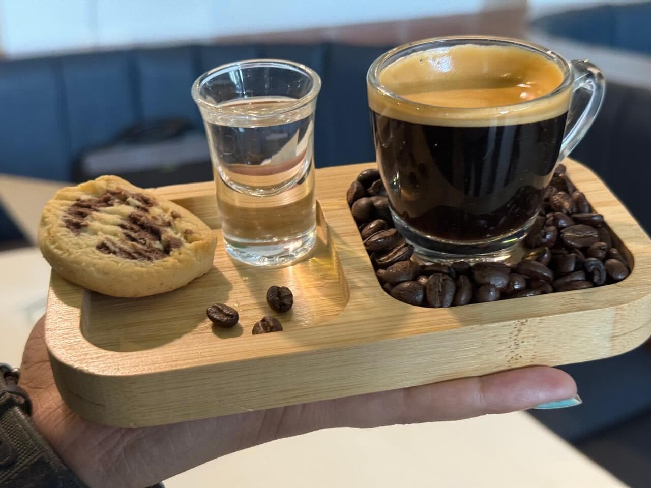 Café lungo with a glass of water and a cookie on a wooden tray